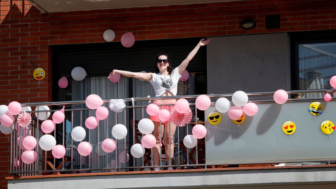 Женщина на балконе, украшенном воздушными шарами и смайлами, в поселке Санта-Маргарида-де-Монбуй неподалеку Барселоны, Испания, 21 марта 2020 года. Из-за карантина жители поселка сидят по домам, а ежедневно в полдень выходят на балконы, чтобы петь и танцевать вместе