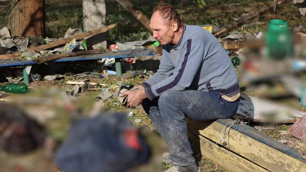 Мужчина сидит рядом с погибшими на месте попадания российской ракеты в кафе-магазин в селе Гроза Харьковской области, 5 октября 2023 года