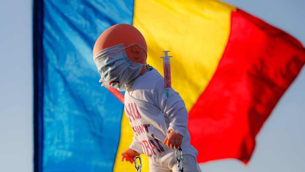 Протестувальники проти вакцинації тримають ляльку з написом «Я не хочу бути лабораторним щуром» на тлі румунського національного прапора під час мітингу біля будівлі парламенту в Бухаресті, Румунія, 7 березня 2021 року