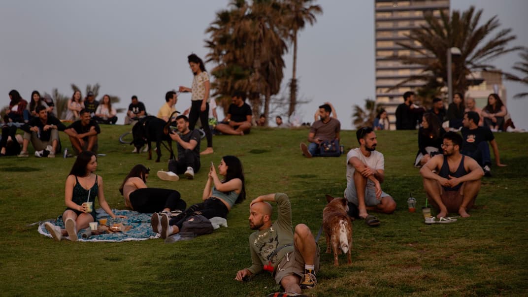 Люди без масок наблюдают за закатом в Тель-Авиве, Израиль, 18 апреля 2021 года. Израиль ослабил карантинные ограничения после кампании массовой вакцинации