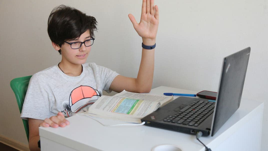 Школьник поднимает руку во время онлайн-урока, учась дома на карантине