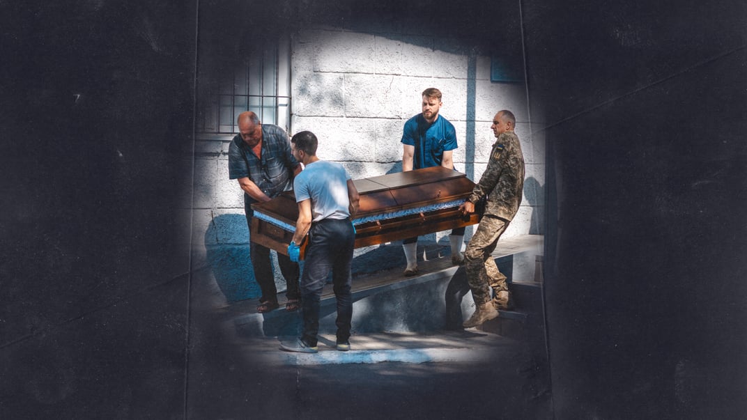 Працівники моргу, водій та родич виносять труну з тілом військового