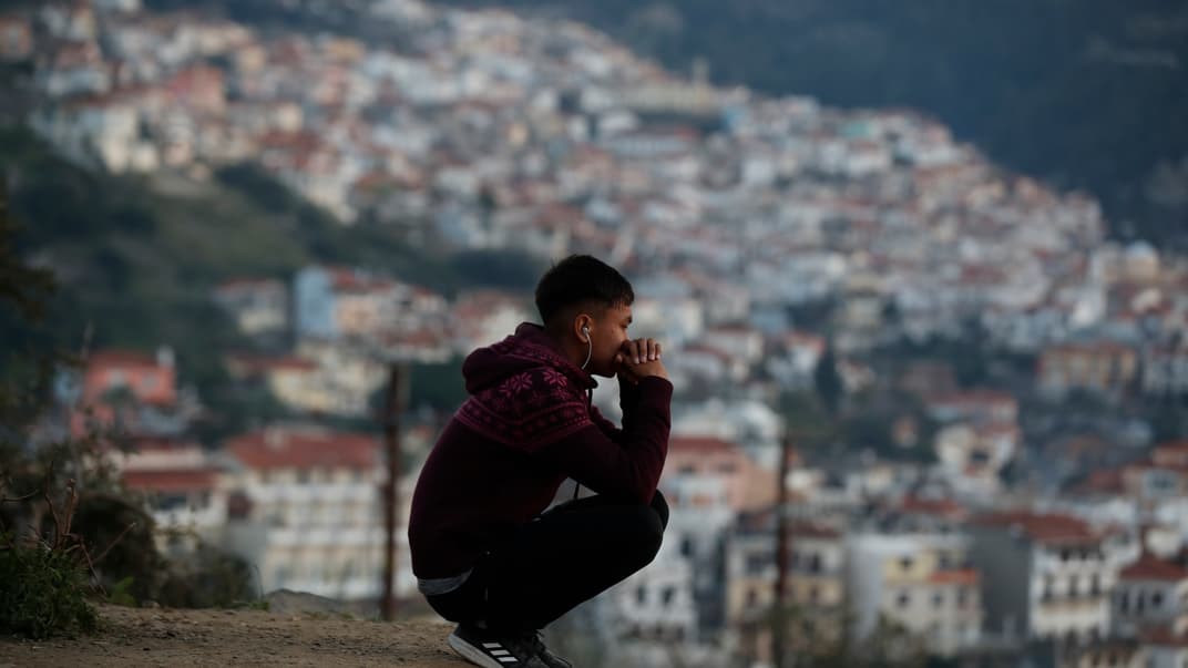 Мальчик-мигрант сидит на холме за периметром переполненного лагеря беженцев в порту Вати на острове Самос в восточном Эгейском море, Греция, 23 февраля 2021 года