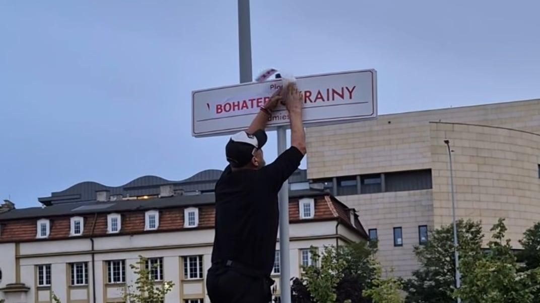 Чоловік заклеює табличку з написом «Площа Вільної України»