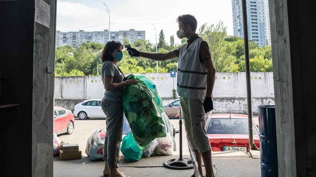 Работник проверяет температуру женщины с пакетами с мусором при входе на станцию сортировки мусора в Киеве