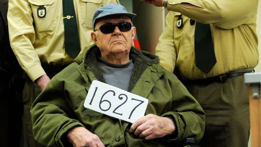 Джон Демьянюк держит табличку 1627 (номер советского следственного досье), в то время как его ввозят в зал суда в Мюнхене, Германия, 22 февраля 2011 года