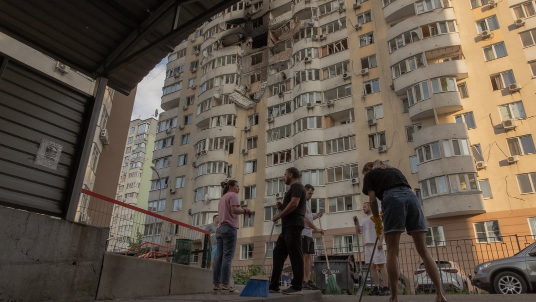 Люди убирают завалы перед жилым домом, поврежденным во время российского авиаудара в Киеве 6 июня 2025 года