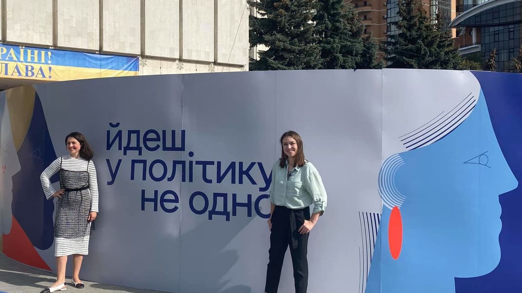 Активістка Євгенія Кулеба, яка очолила список «Слуги народу» на виборах до Київради, разом із іншою активісткою Ксенією Симоновою, яка балотувалася до Київради по Солом'янському району, позують на фоні плакату біля будівлі ЦВК. 