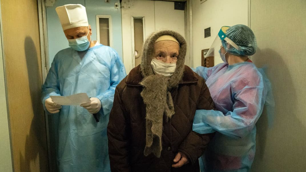 Двоє медичних працівників проводжають літню жінку, яка хворіє на COVID-19, до лікарні в Коломиї, Західна Україна, 23 лютого 2021 року