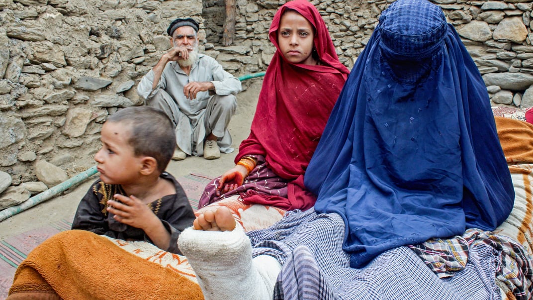 Афганська жінка в паранджі з травмованою ногою сидить поруч із дітьми біля будинку після землетрусу в окрузі Дара-і-Нур провінції Нангархар, 3 вересня 2025 року