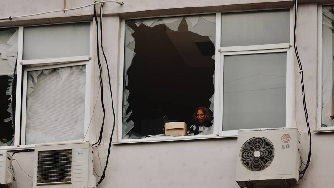 Жінка виглядає з пошкодженого вікна будинку в Одесі після російської атаки, 12 лютого 2026 року