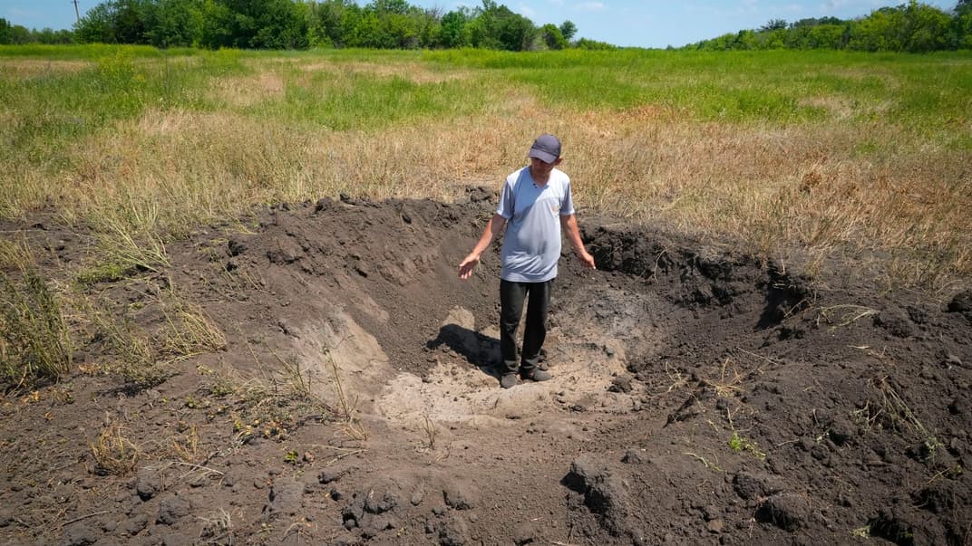 Місцевий виробник зерна показує вирву, залишену російським снарядом на полі в селі Птиче Донецької області, 12 червня 2022 року