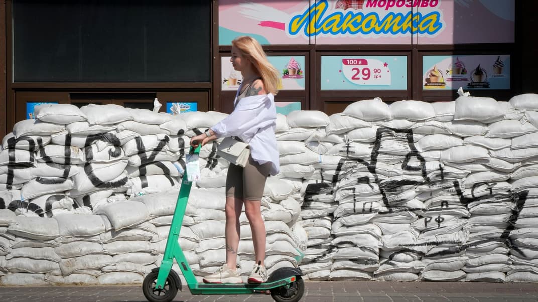 Дівчина проїжджає на самокаті біля мішків з піском у центрі Києва, 7 червня 2022 року