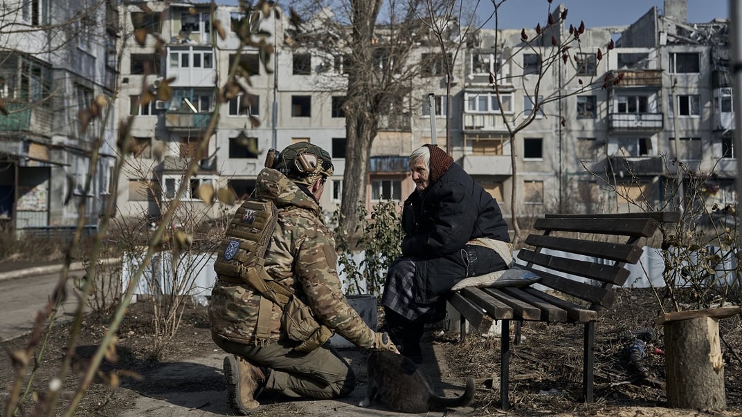 Ілюстративне фото. Літня жінка сидить в оточенні пошкоджених будинків у Покровську, а капелан переконує її евакуюватися, 14 лютого 2025 року