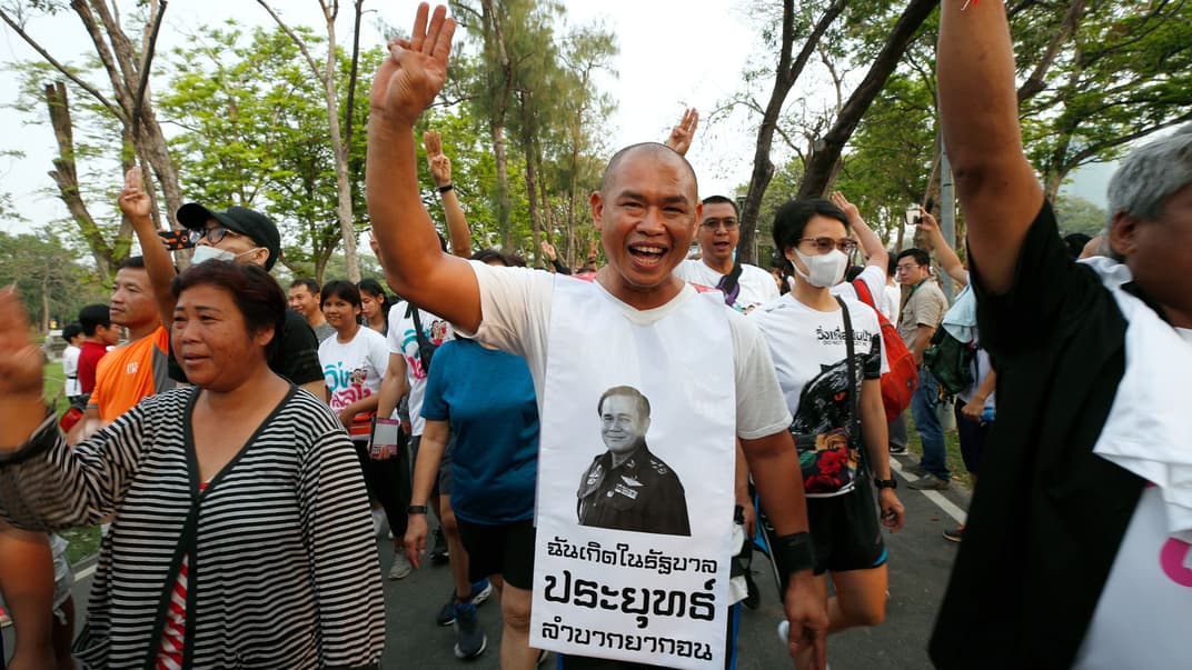 Антиурядовий протестувальник вдягнений у фартушок із портретом прем'єр-міністра Таїланду Праюта Чан-Очи та показує символічний жест єдності трьома пальцями разом зі своїми однодумцями на Забігові проти диктатури в Бангкоку, Таїланд, 12 січня 2020 року