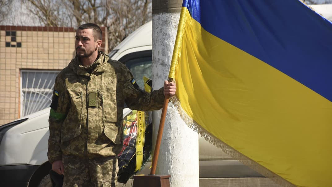 Український військовослужбовець тримає український прапор під час церемонії похорону загиблих в селі Олександрівка Одеської області, 12 квітня 2022 року