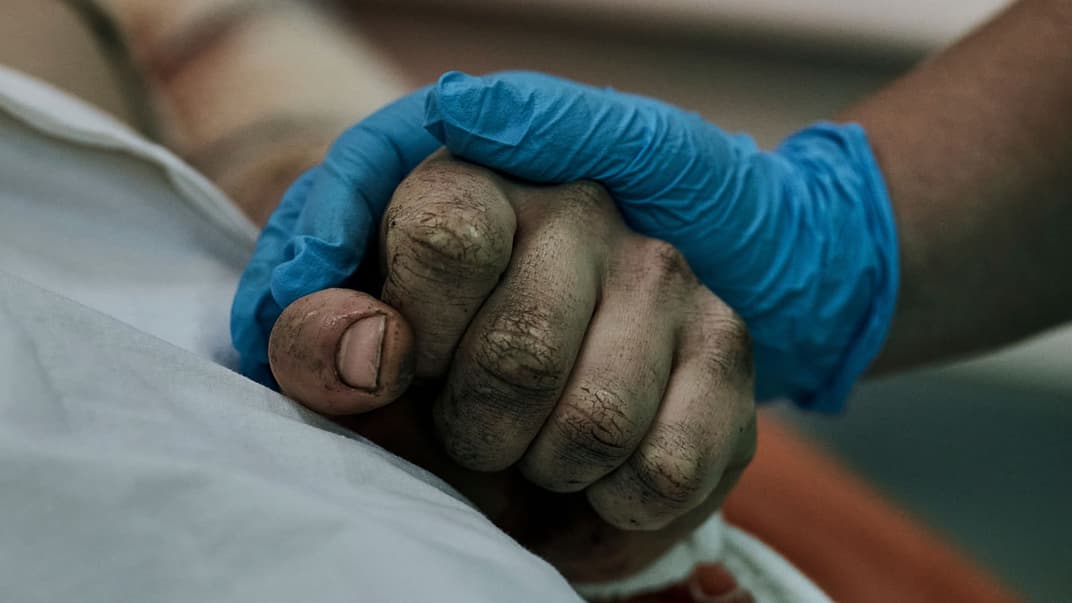 Медик держит за руку украинского военного, раненого в бою с российскими войсками в городской больнице в Николаеве, 3 ноября 2022 года