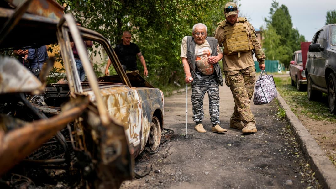 Волонтер допомагає чоловікові, який виходить із дому в будівлі, пошкодженій ракетним ударом у Слов’янську, 31 травня 2022 року