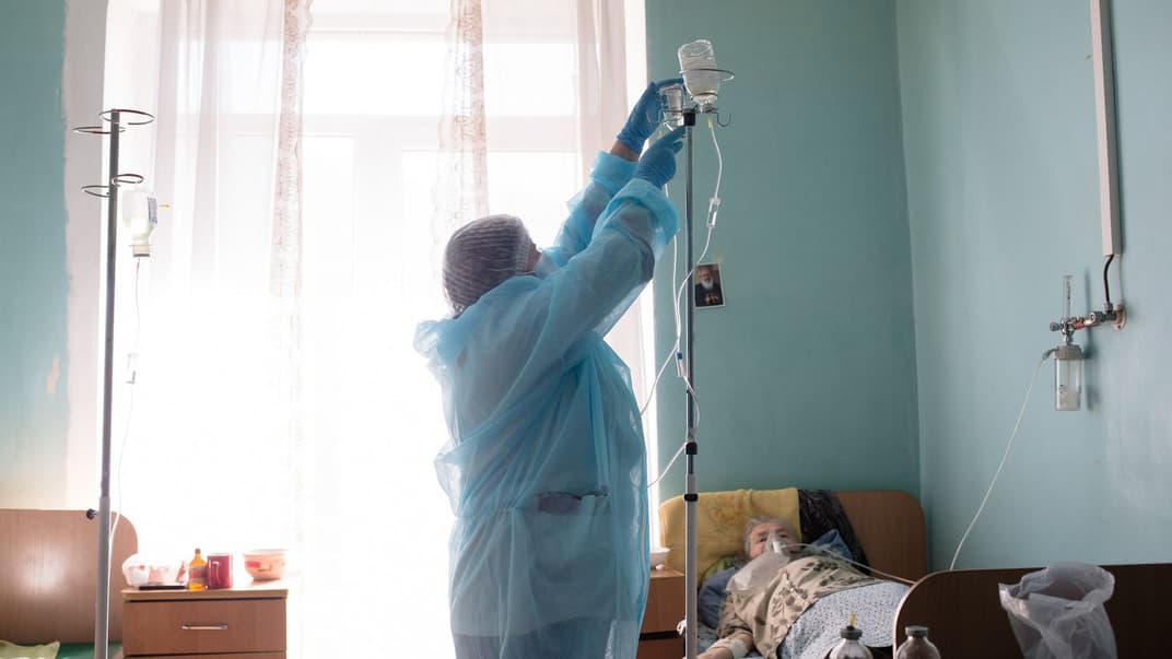 Медсестра встановлює крапельницю жінці з коронавірусом, яка лежить у палаті для інфекційних хворих у лікарні міста Яремче на Івано-Франківщині