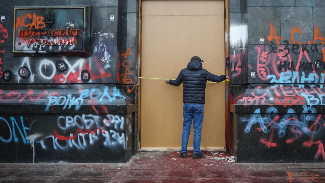 Мужчина измеряет ширину центральных дверей в здании Офиса президента 22 марта 2021 года. Стекло на центральных дверях было разбито во время акции протеста 20 марта, в день рождения Сергея Стерненко