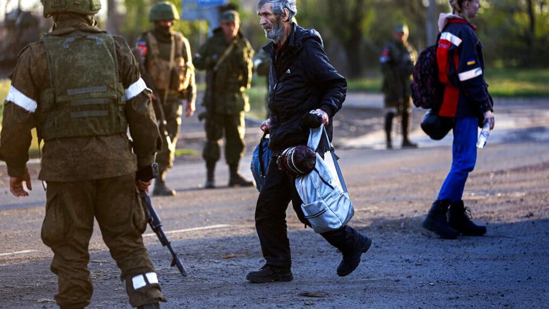 Мирний житель, який вибрався з «Азовсталі», йде до автобуса повз російських військових, 6 травня 2022 року