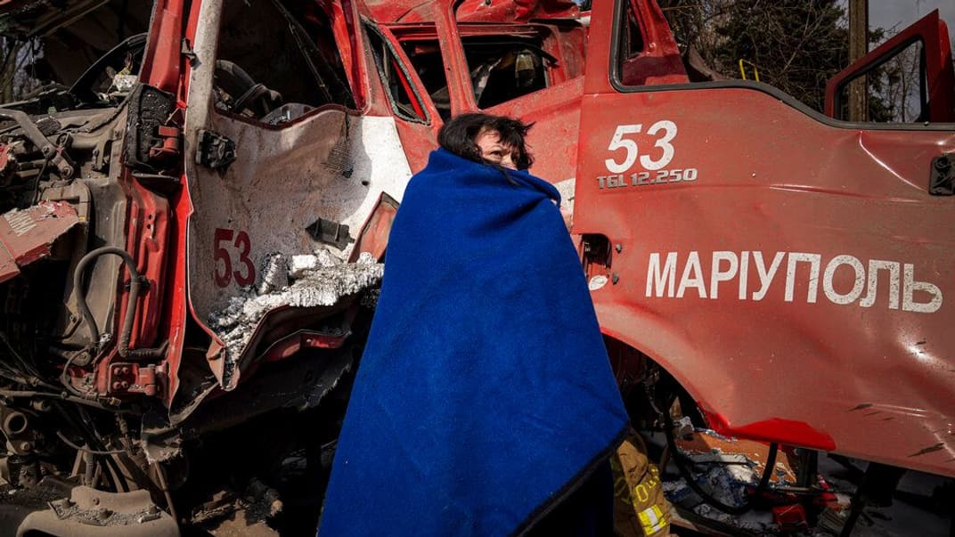 Жінка вкривається ковдрою біля обстріляної пожежної машини. 10 березня 2022 року