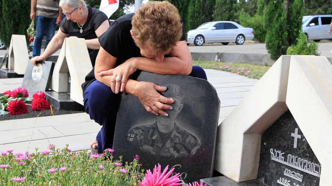 Женщина сидит над могилой родственника, погибшего солдата, во время церемонии возложения венков к 10-й годовщине российско-грузинской войны, Тбилиси, Грузия, 8 августа 2018 года