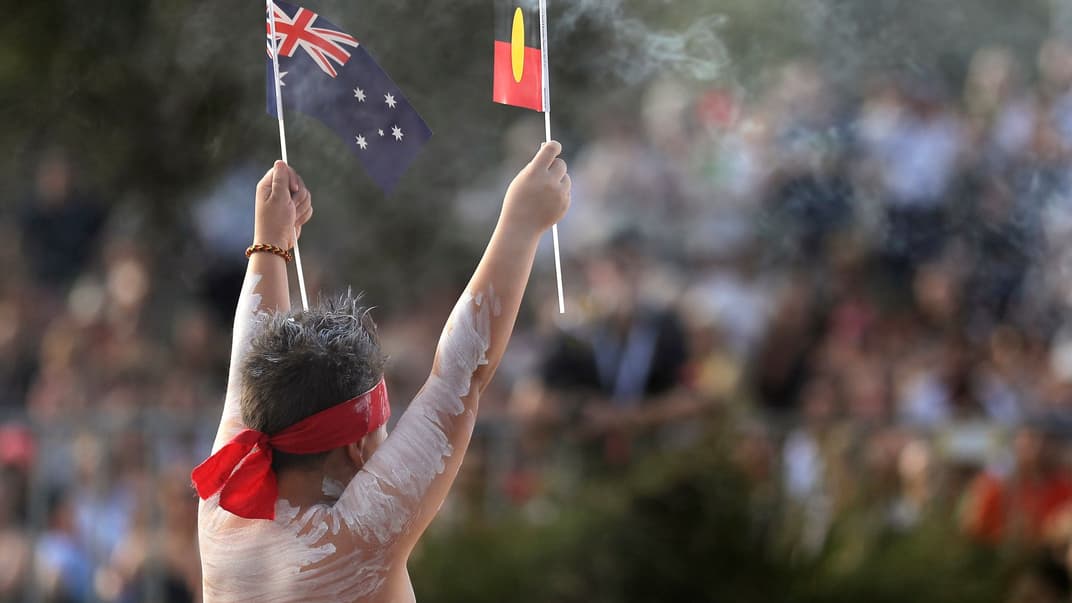 Парень из коренного населения Австралии держит флаг своего племени и флаг Австралии во время празднования. Сидней, Австралия, 26 января 2020 года