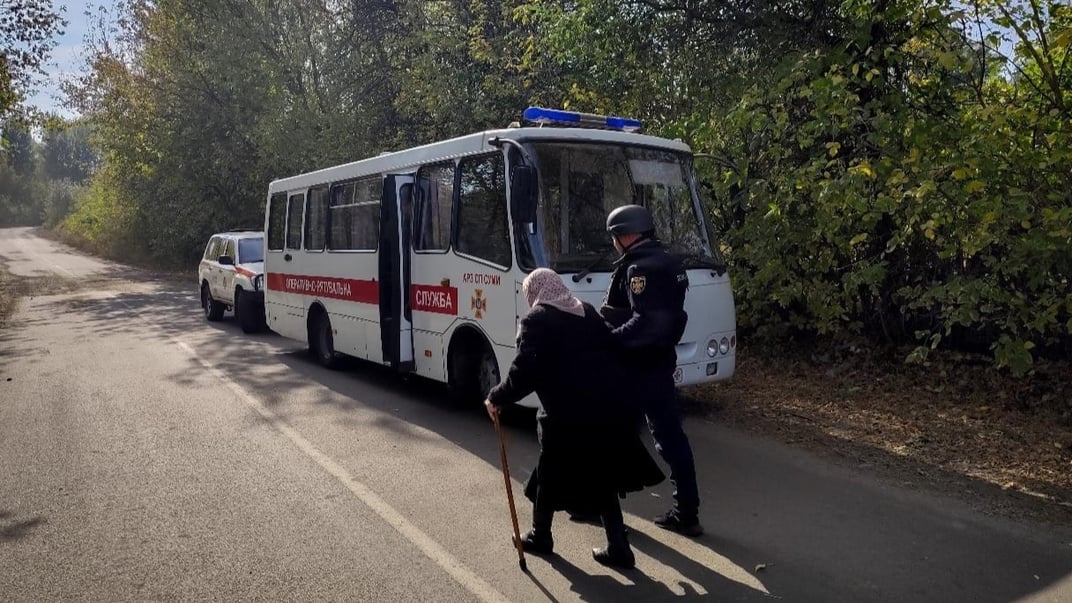 Спасатель помогает пожилой женщине эвакуироваться в Сумской области