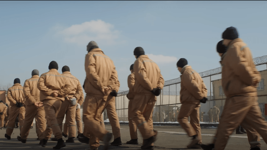 Тримаючи руки за спиною, в'язні один за одним крокують у напрямку їдальні