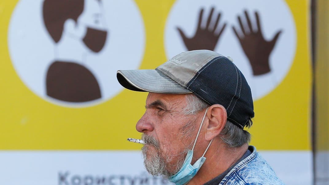 Украинец курит перед плакатом о мерах во время пандемии коронавируса COVID-19 в Киеве, Украина, 8 сентября 2020 года.