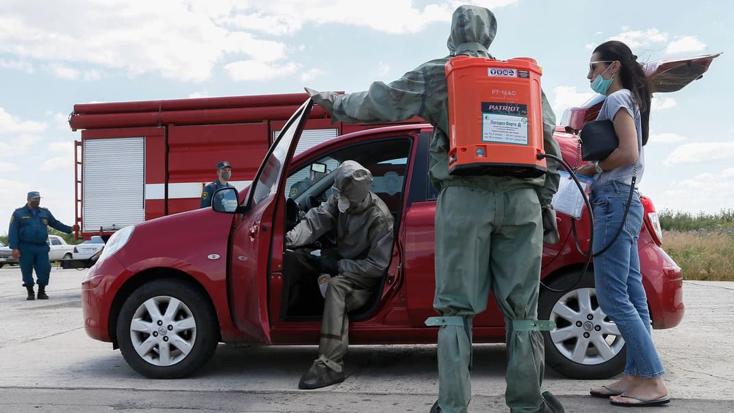 Чоловіки в захисних костюмах дезинфікують автомобіль жінки, яка перетинає блокпост в «ДНР»