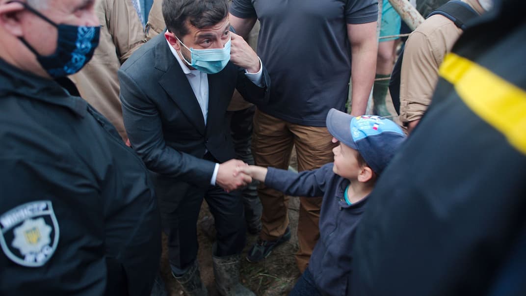 Президент України Володимир Зеленський (в центрі) тисне руку місцевому хлопчику у селищі Ланчин на Прикарпатті, що постраждало від повені, Івано-Франківська область, 25 червня 2020 року. Ліворуч — міністр внутрішній справ Арсен Аваков