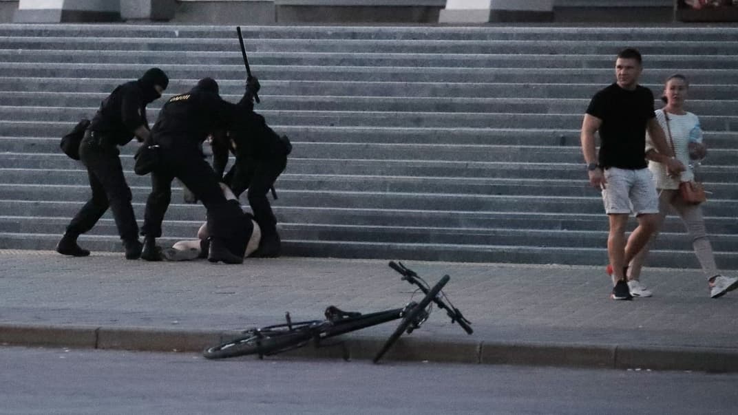 Правоохоронці б'ють і затримують невідомого протестувальника в Мінську, Білорусь, 10 серпня 2020 року. Поруч повз проходить пара