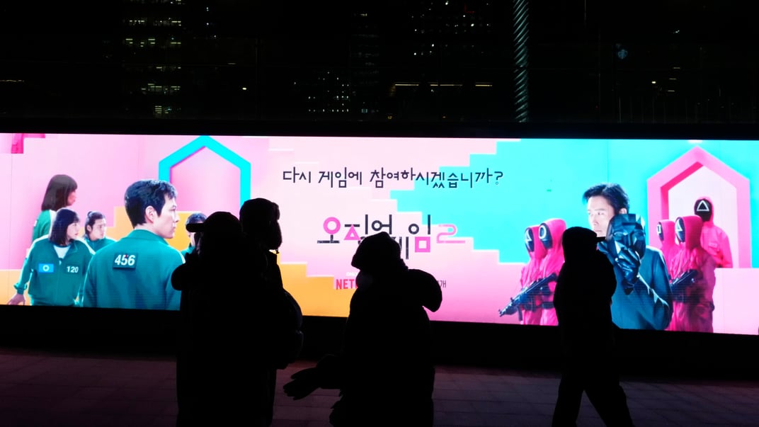 Люди проходят мимо рекламы второго сезона «Игры в кальмара» в Сеуле