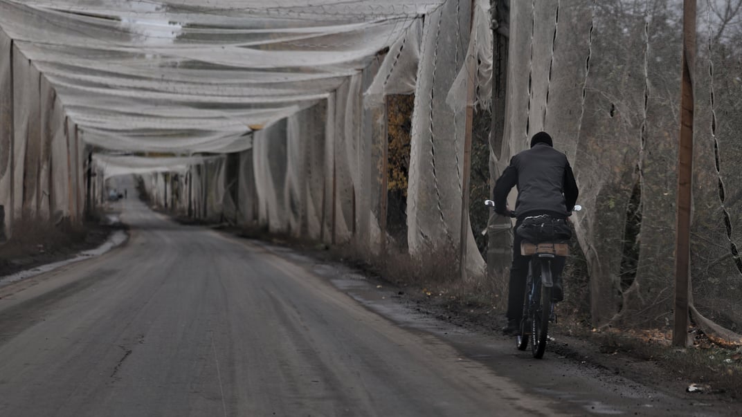 Чоловік їде на велосипеді дорогою, вкритою антидроновою сіткою в Костянтинівці на Донеччині,  1 листопада 2025 року