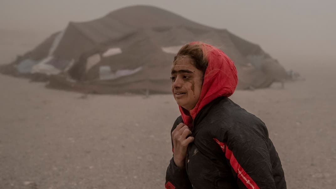 Афганская девушка несет полученную помощь к своей палатке и плачет от сильной песчаной бури после землетрясения, 12 октября 2023 года