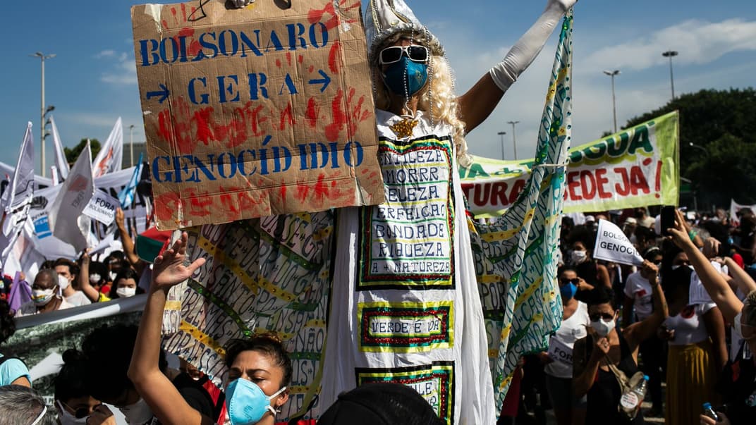 Протестующий держит плакат «Болсонару совершает геноцид» на акции протеста в Рио-де-Жанейро, 29 мая 2021 года