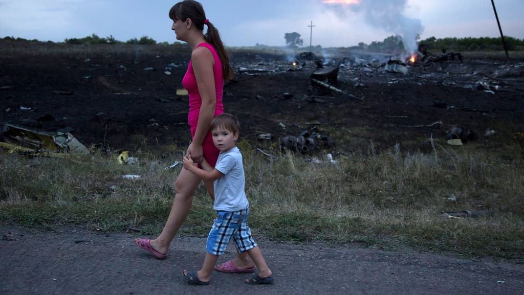 Женщина с ребенком проходят мимо места крушения пассажирского самолета возле села Грабово, Украина, 17 июля 2014 года