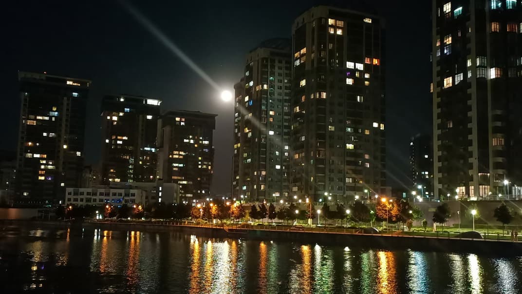 Освещенная вечером набережная возле ТРЦ River Mall в Киеве, 14 июля 2023 года