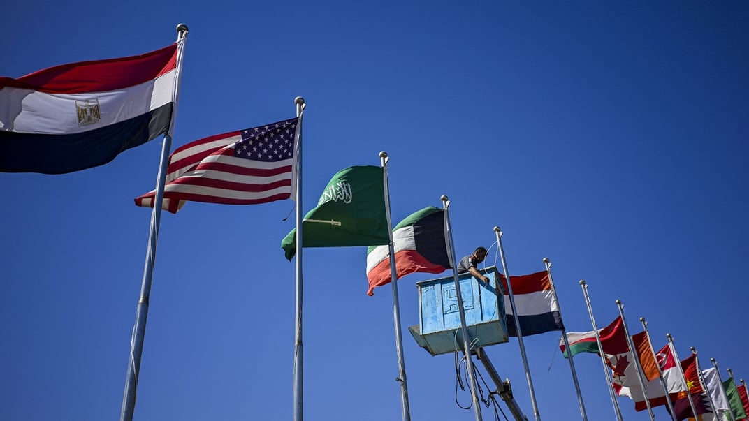 Комунальник піднімає прапори різних країн біля міжнародного аеропорту Шарм-ель-Шейха перед прибуттям світових лідерів на саміт, 11 жовтня 2025 року