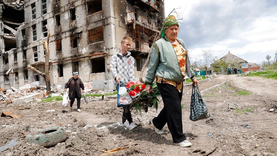 Жителі Маріуполя проходять повз зруйнований житловий будинок, 2 травня 2022 року