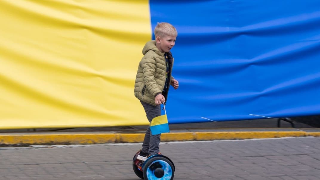 Хлопчик катається на гіроскутері на тлі прапора України у Києві, 30 травня 2022 року