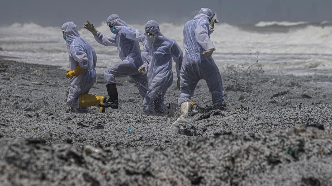 Люди в защитных костюмах среди мусора, который вымыло на берег с горевшего судна, Коломбо, Шри-Ланка, 27 мая 2021 года