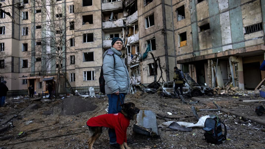 Жінка із собакою стоїть біля зруйнованої будівлі у Києві, 20 березня 2022 року