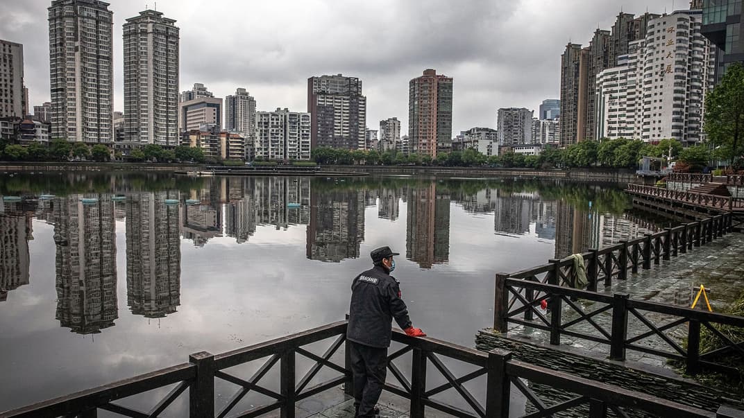 Охоронець громадського порядку у захисній масці для обличчя стоїть біля озера у місті Ухань, Китай, 29 березня 2020 року
