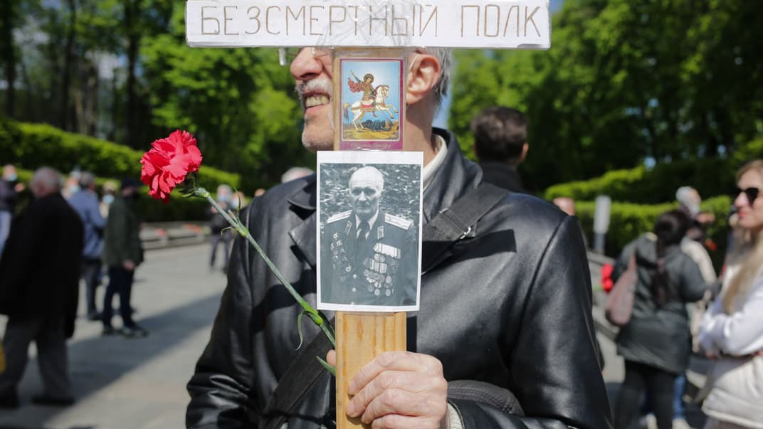 Учасник акції з ушанування пам'яті ветеранів Другої світової війни стоїть із портретом ветерана та квіткою біля Вічного вогню в Парку слави