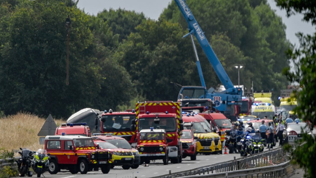 Кран підіймає пошкоджений автобус, в якому їхали дорослі та підлітки з України. Навколо працюють рятувальники, поліція та офіцери жандармерії