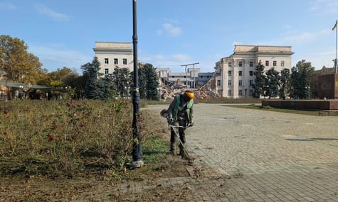 Чоловік косить траву на фоні зруйнованої будівлі в Херсоні