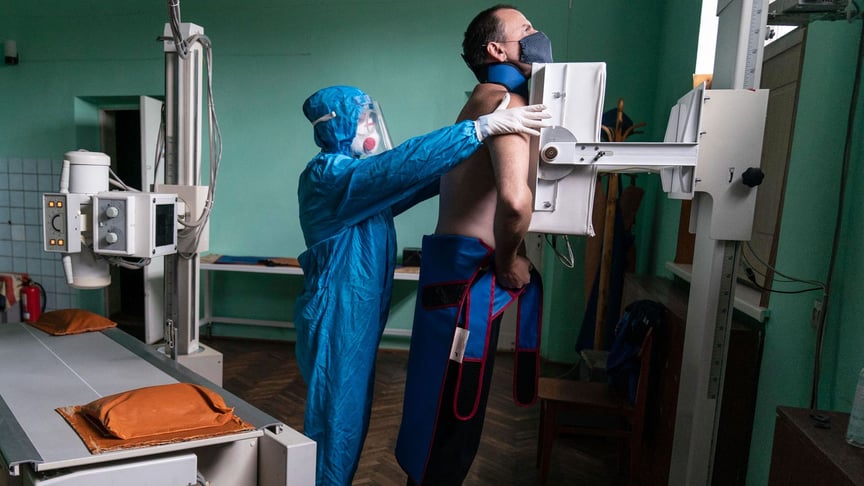 Медик, одягнений у спеціальний костюм для захисту від коронавірусу, готує пацієнта з коронавірусом до рентгенографії легенів у міській лікарні в Стрию, Україна.